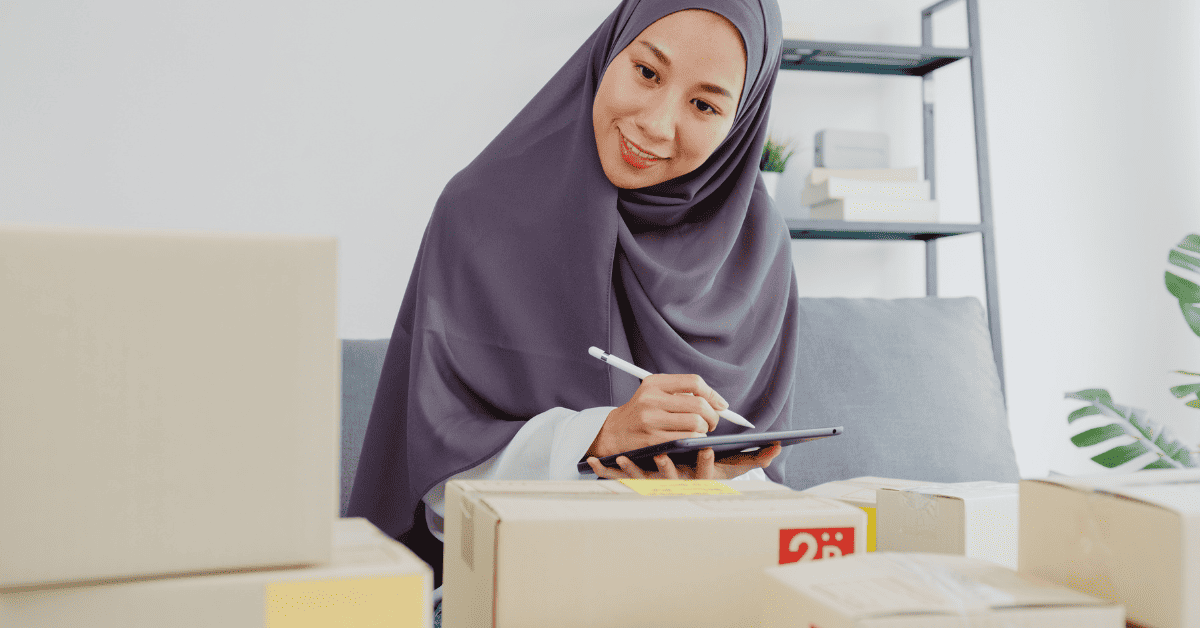 Young Asia muslim businesswoman check product purchase order on stock and save to tablet computer work at home office. Small business owner, online market delivery, lifestyle freelance concept.